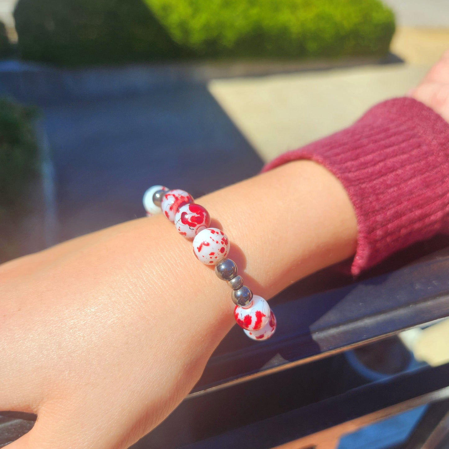 Close-up of a wrist wearing a colorful beaded bracelet with a blurred outdoor background.